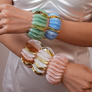 Detail of colorful acrylic stretch bracelets with gold accents on model's wrist