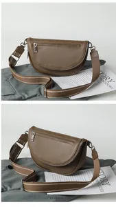 Detail view of brown semi-circular crossbody bag with litchi texture and canvas strap