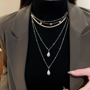 Detail of layered gold necklace featuring water drop pearls on a green blazer outfit