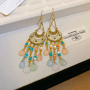 Detail of Bohemian gold earrings featuring white enamel crescents and colorful beaded tassels