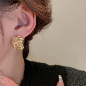 Macro detail of textured gold irregular square earrings on a model showing modern metal design