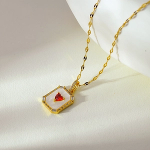 Macro detail of gold rectangle necklace with white shell inlay and red heart gemstone