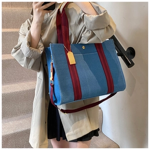Detail of blue denim tote bag with red-brown striped strap and gold rose charm accessory