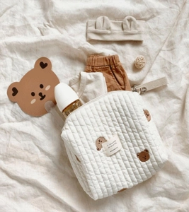 Detailed flat lay of a beige quilted cotton diaper bag with cute bear embroidery decor