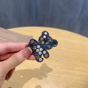 Close-up of teddy bear hair clip with sparkling blue and gold rhinestones held by hand
