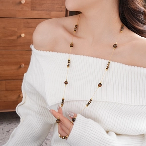 Vue détaillée du collier long doré avec perles œil de tigre sur un pull blanc