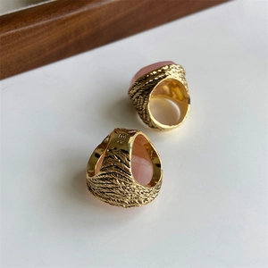 Detail of gold metal rings featuring pink oval crystals and feather texture engravings