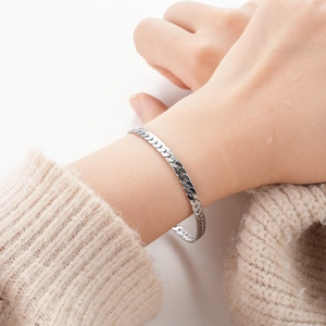 Macro shot of silver flat curb chain bracelet on wrist showing polished finish