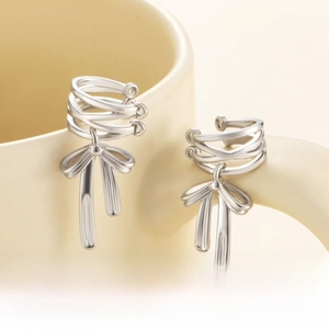 Detail of silver bow pendant ear cuff hanging on a beige ceramic mug rim