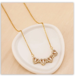 Close-up of golden clover necklace with heart pendants and crystals on a white ceramic dish