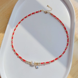 Détail du collier avec œil maléfique, perles rouges et perle d'eau douce sur plateau