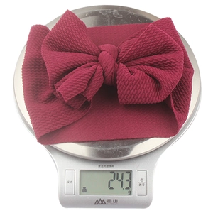 Detail view of burgundy waffle knit baby headband with bow on a digital scale 24.3g