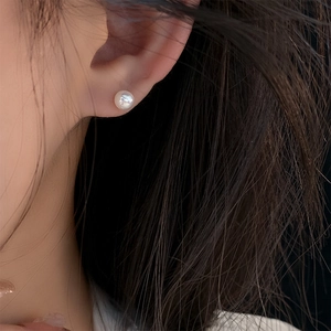 Close-up of a white freshwater pearl stud earring worn on a model's ear showing luster