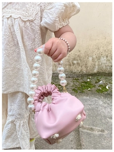 Close-up of pink pleated cloud bag with large pearl handle held by a child