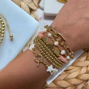 Detail of layered gold beaded bracelets with pearls and heart charms on a stone surface