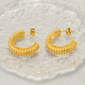 Close-up of golden C-shaped textured earrings on a glass plate with silk background
