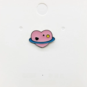 Detailed macro view of an enamel pink heart planet brooch with blue rings on a card