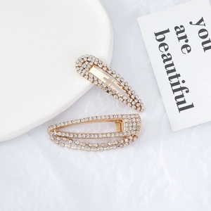 Detailed view of golden metal hair clips with sparkling rhinestones on a white background