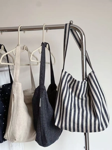 Close-up of assorted canvas tote bags in striped, polka dot, and solid linen hanging on a rack