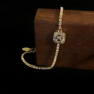 Detailed close-up of a gold tennis bracelet featuring a square radiant-cut center stone