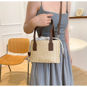 Detail of woven straw bucket bag featuring brown leather handles and drawstring closure