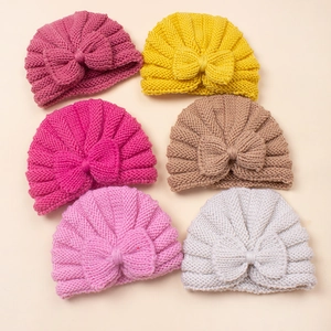 Flat lay display of baby knitted hats with bow details in six vibrant warm colors