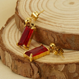 Elegant 18K gold plated earrings with rectangular red gemstones on a rustic wood base