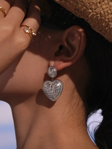 Close-up of a silver heart earring with textured finish worn on ear in sunlight