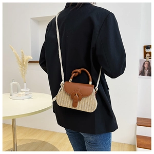 Detail of woven straw handbag featuring brown leather trim and cotton rope strap