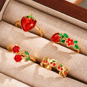 Detail of four gold fruit rings featuring red strawberry and cherry enamel designs