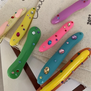 Detail showing wavy resin hair clips with colorful rhinestones on a canvas texture