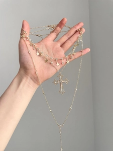 Detailed close-up of a layered gold necklace featuring crystal cross and star pendants