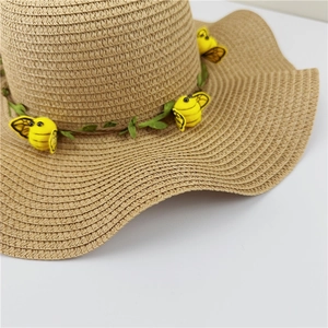 Détail d'un chapeau de paille à bord ondulé avec des abeilles et une guirlande de feuilles