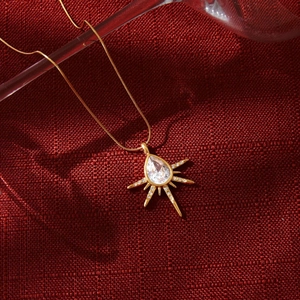 Collier doré avec pendentif soleil et zircone goutte sur tissu texturé rouge