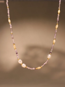Macro detail of handmade beaded necklace with purple crystals, pearls and gold heart charm