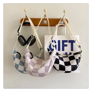 Three checkered crossbody bags in blue, purple, and black hanging on wooden hooks