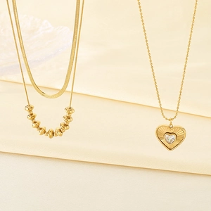 Detail of layered gold beaded snake chain and heart pendant necklace with crystal