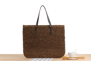 Close-up of handmade brown straw tote bag featuring reinforced dark leather handles