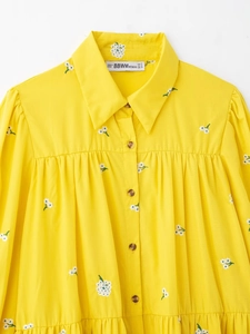 Close-up of yellow embroidered shirt featuring white floral patterns and polo collar detail