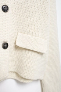Gros plan détaillé du cardigan en maille crème avec boutons foncés et poche texturée