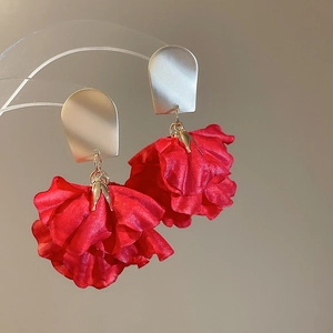 Close-up of red fabric floral petals with matte gold hoop earrings on acrylic stand
