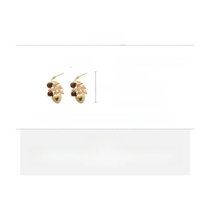 Detail view of heart-shaped gold tassel earrings with tiger eye beads and silver pins
