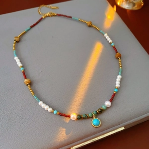 Detail of bohemian pearl necklace with turquoise beads and gold pendant on gray background