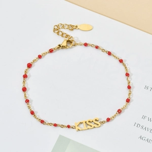 Macro shot of gold-plated KISS letter pendant bracelet with red beads and lobster clasp