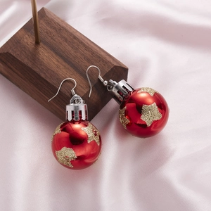 Detail of red Christmas bulb earring with golden stars on silk and wooden stand