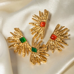 Detailed shot of gold plated sunburst earrings with red and green gemstones on silk
