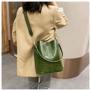 Detail of dark green crocodile texture bucket bag with wide strap on model