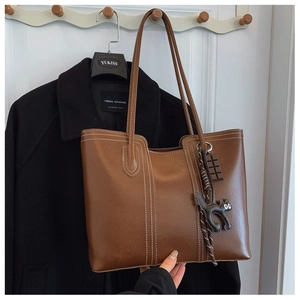 Detailed view of a brown leather tote bag featuring white contrast stitching and cat charms