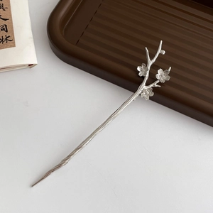 Detail of silver branch hairpin with plum blossom decor on a minimalist tray