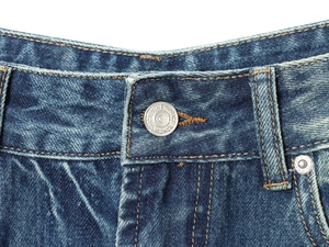 Detailed close-up of waistband with metal button and stitching on dark blue denim jeans